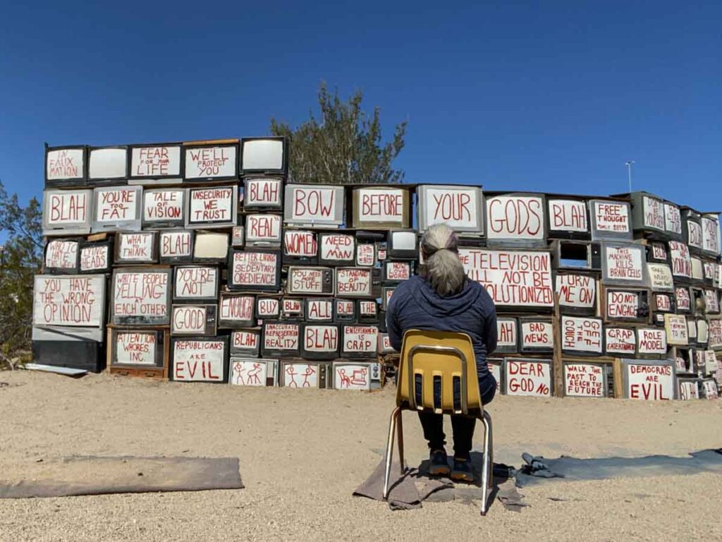 TV wall at East Jesus, California. Woman sitting in a chair